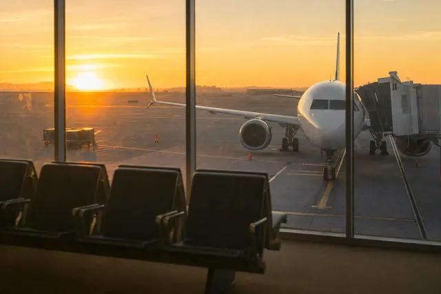 A plane at the gate, seen through an airport window at sunrise.