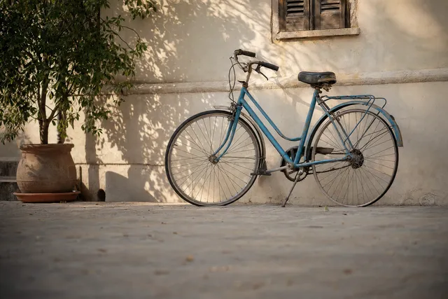 An old blue bicycle leaning against a sunlit wall.