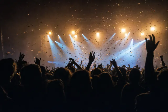 Hands up in a crowd at a gig, under stage lights and falling confetti.