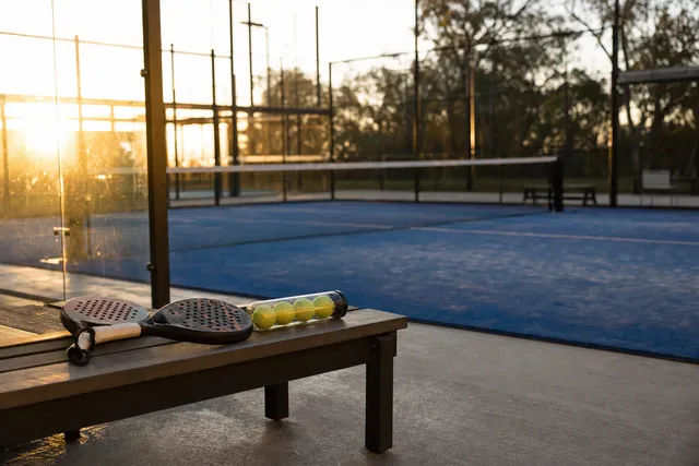 An empty padel court at sunset, with two rackets on a bench.