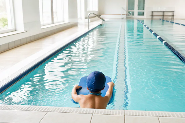 A child at the edge of an indoor pool lane, seen from behind.